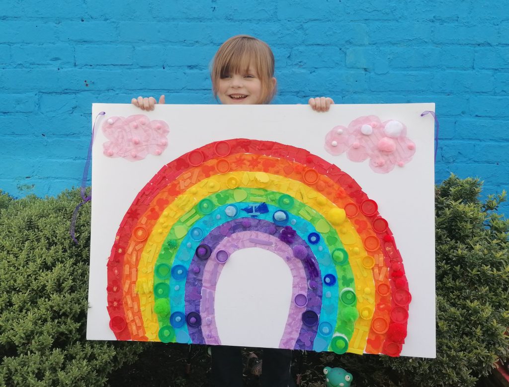 LHL_2020_021a: Photograph of Isla holding a large rainbow sign which she made.