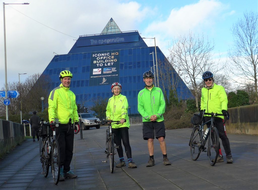 REF_1231b: photograph of four people with the blue Stockport pyramid building behind them.