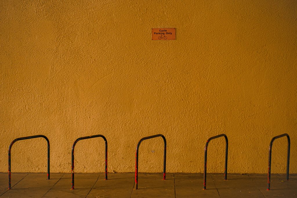 STOPM_2020_418e: Photograph of a mustard yellow wall, with a bike rack in the foreground, taken by Jake Bowden.